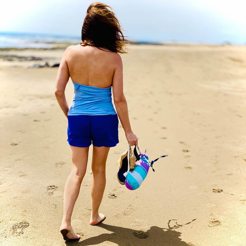 girl wandering along beach carrying talia hammam towel in carry pouch