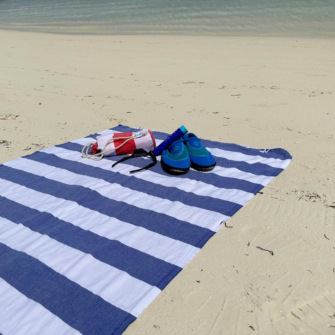 Blue and white striped towel on a sandy beach with shoes and a bag.