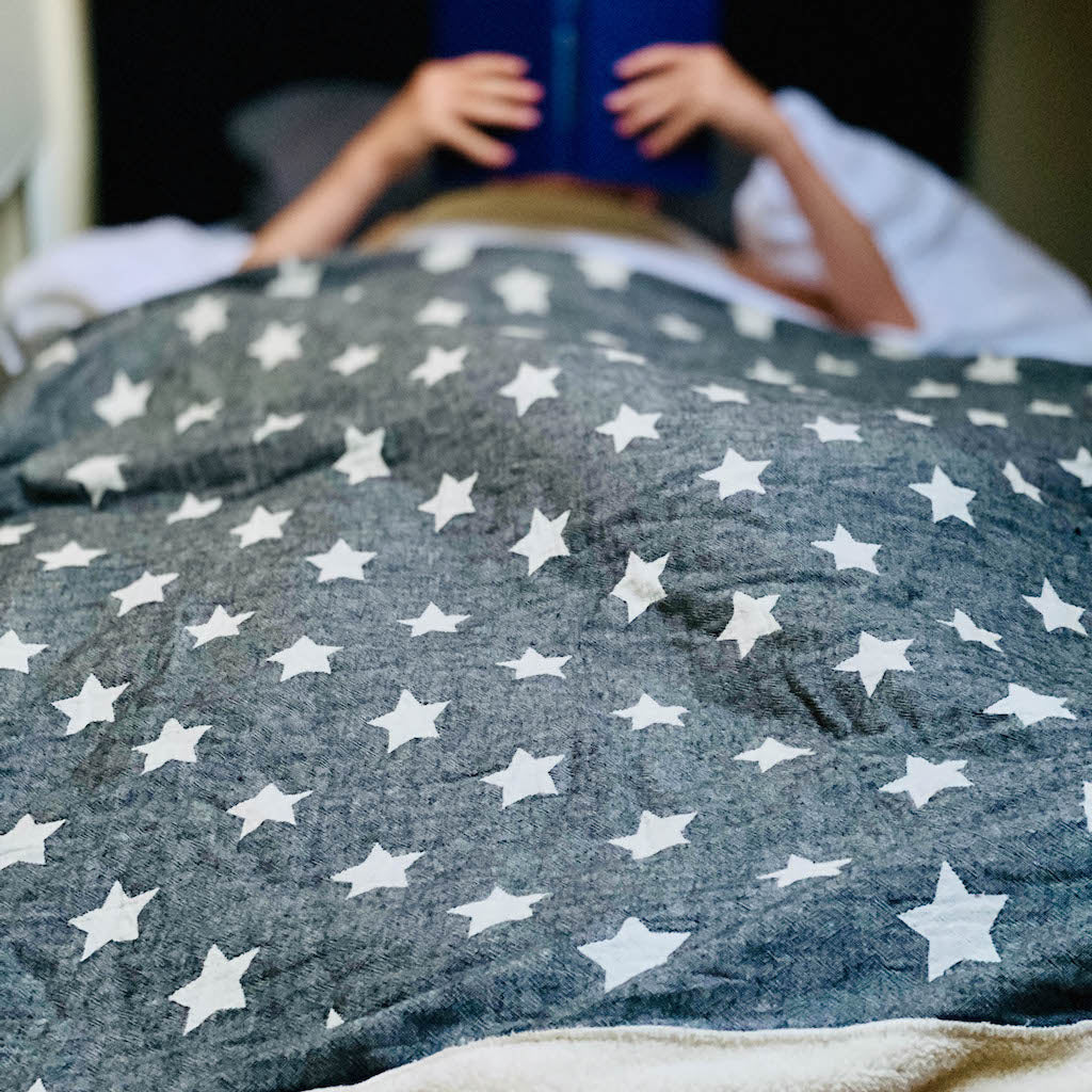 Girl reading in bed under charcoal star fleece lined throw