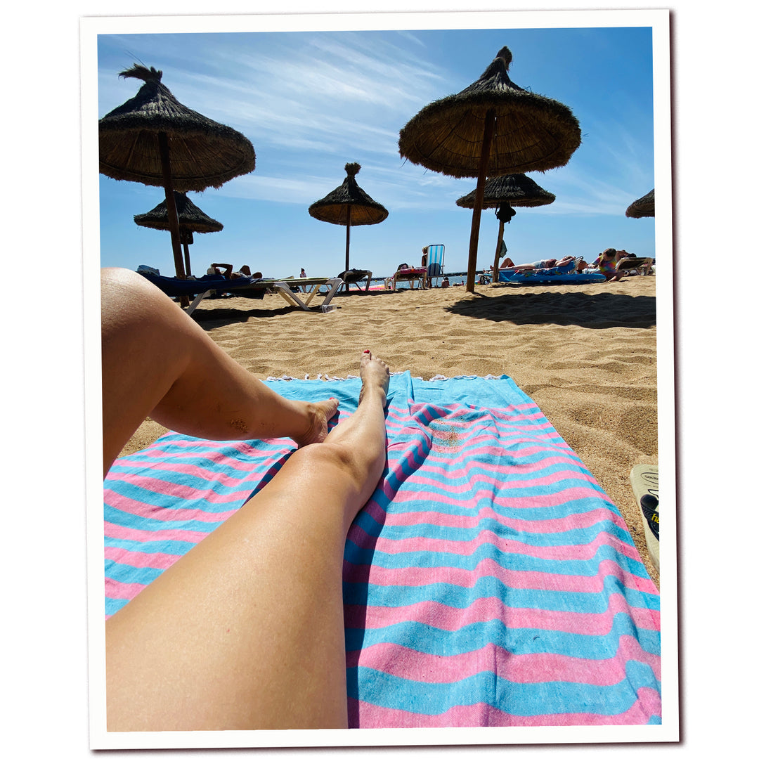 lady lying on clara hammam towel on beach with parasols