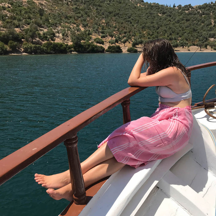 girl sitting on edge of boat using pink perim hammam towel as a wrap