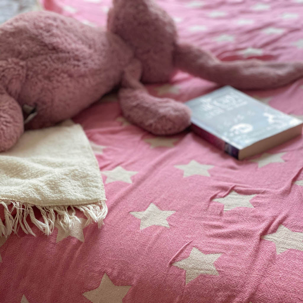 Child's book and soft toy on pink fleece lined throw on bed